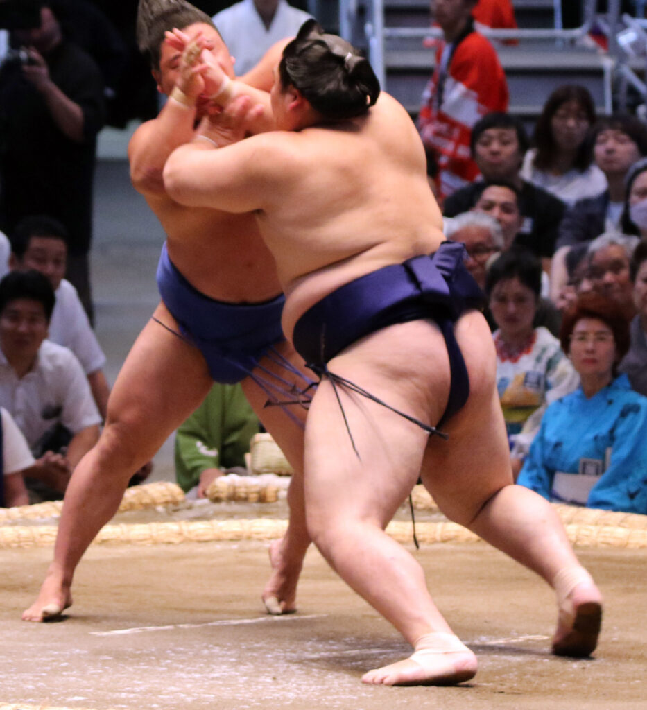 Two sumo wrestlers locked chest to chest near the edge of the ring